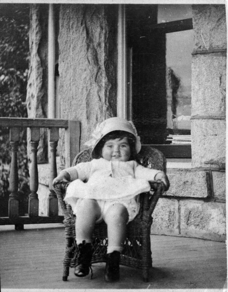Cecily R. Hunt, a small child in a bonnet, on the porch of a house at 7th Avenue and Birch Street