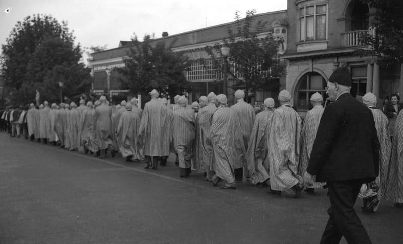 Shriners in striped robes marching in a parade on Burrard Street