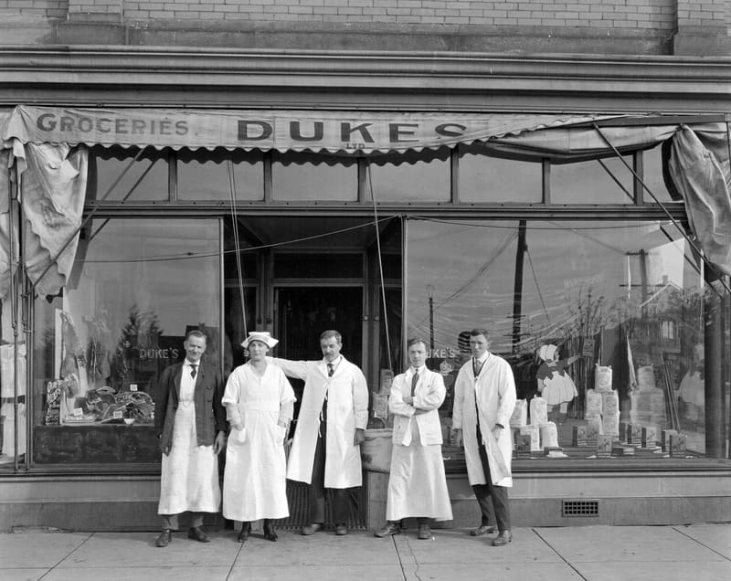The staff of Duke's Grocery in their aprons and coats outside the store at 1588 Commercial Drive