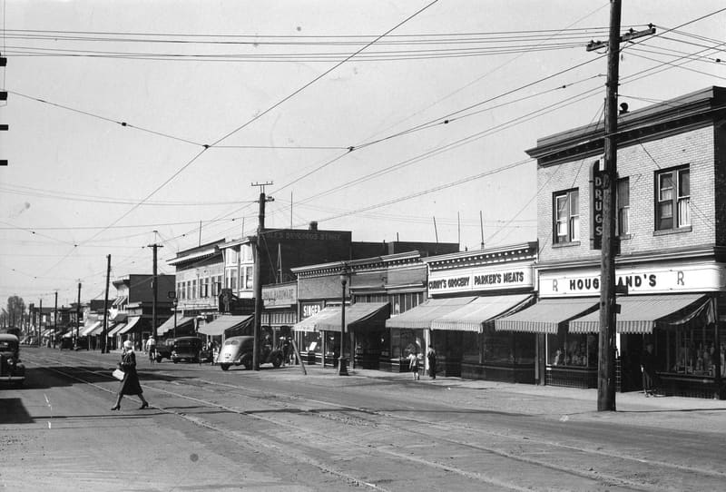The shops on the west side of the 6100 block of Fraser Street, looking south, as a woman crosses the road