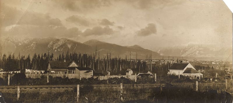 Houses and cleared land seen from 6th Avenue and Maple Street, with the mountains beyond