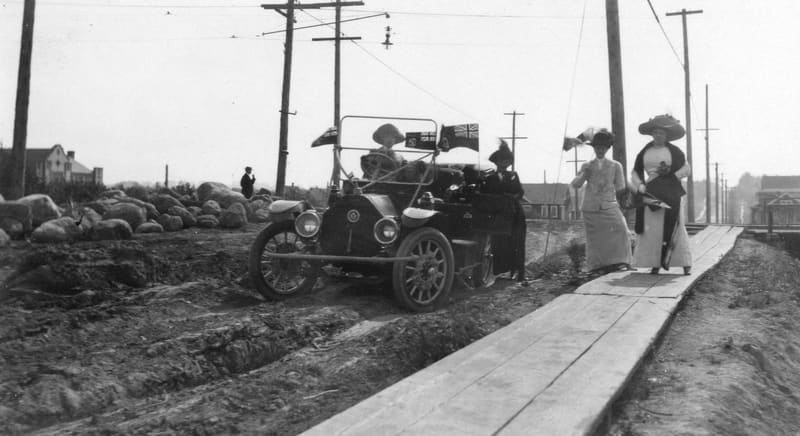 Women beside a car on unpaved Maple Street, among them Maud Boscawen Matthews, with a plank sidewalk beside it
