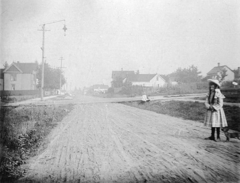 A girl at the dirt crossing of 10th Avenue and Quebec Street, looking east along 10th